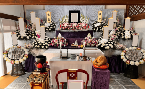 寺院本堂での家族葬の祭壇　ピンクメインのお花で2段飾り 供花が10基飾られている。他に盛籠が2基ある。祭壇の生花は温かみがある色合い